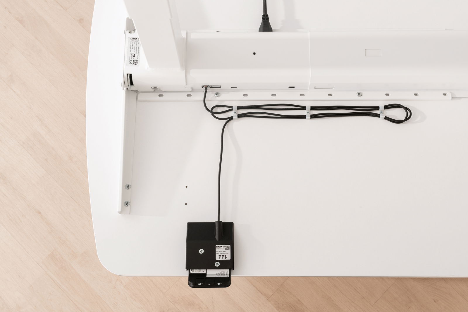 Draufsicht auf die Unterseite eines weißen Schreibtisches mit Kabelmanagement und elektrischen Komponenten.