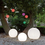 Drei leuchtende Kugelleuchten BULY 30 im Freien, umgeben von Bäumen und bunten hängenden Kugeln, aus der Perspektive von vorne.