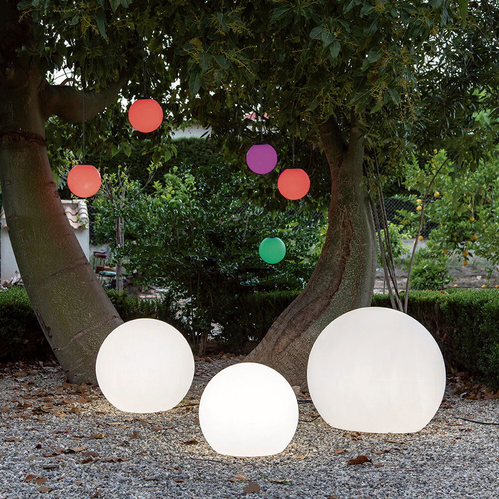 Drei leuchtende Kugelleuchten BULY 30 im Freien, umgeben von Bäumen und bunten hängenden Kugeln, aus der Perspektive von vorne.