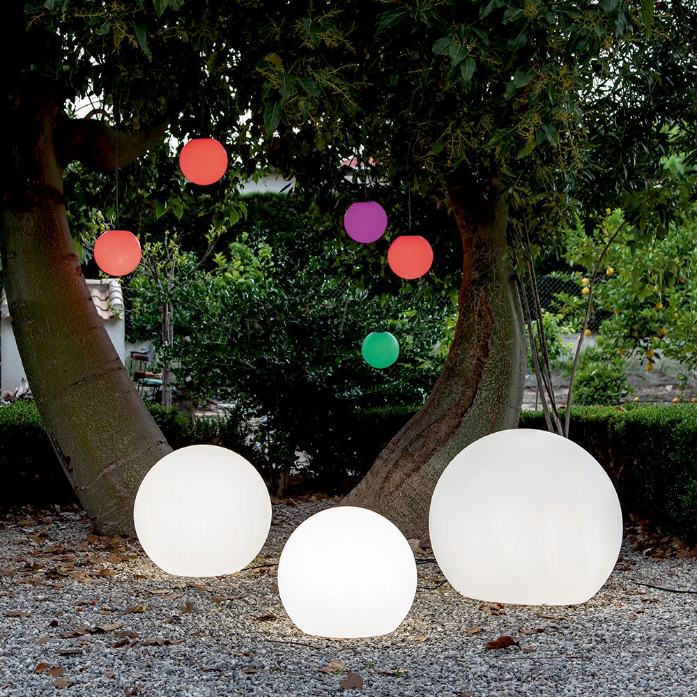 Drei leuchtende Kugelleuchten BULY 30 im Freien, umgeben von Bäumen und bunten hängenden Kugeln, aus der Perspektive von vorne.