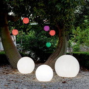 Drei leuchtende Kugelleuchten BULY 30 im Freien, umgeben von Bäumen und bunten hängenden Kugeln, aus der Perspektive von vorne.