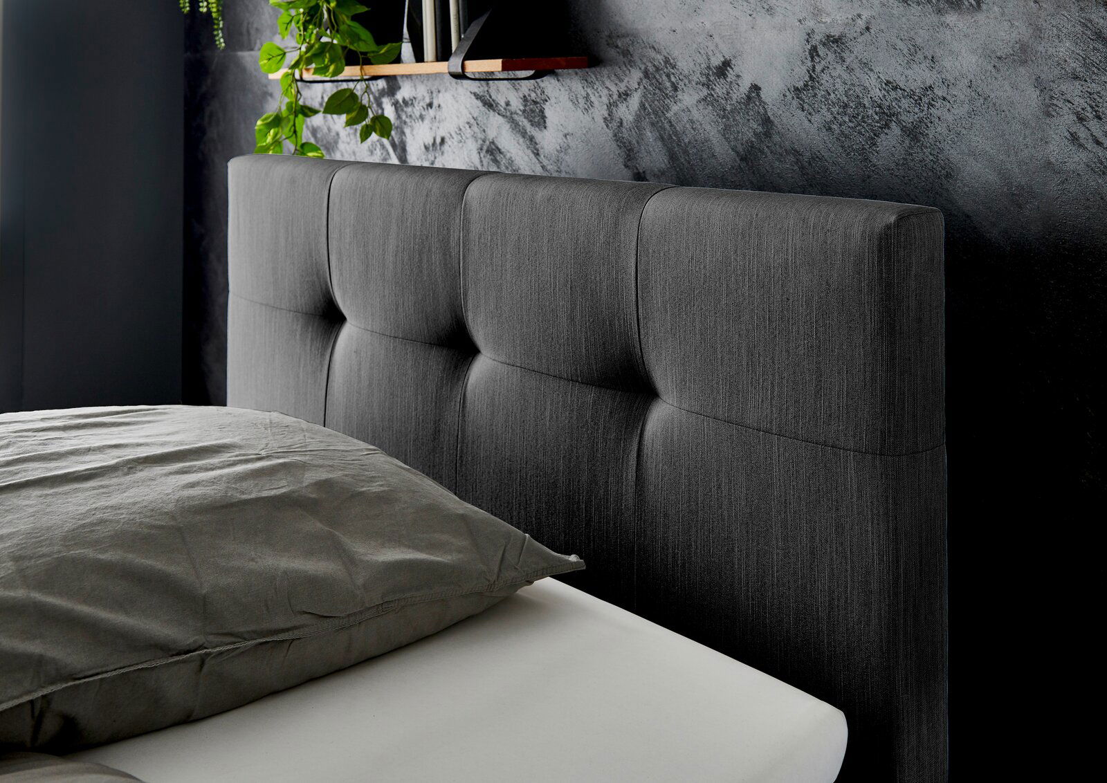 Nahaufnahme eines grauen Boxspringbett-Kopfteil mit gepolstertem Design, seitliche Perspektive