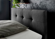 Nahaufnahme eines grauen Boxspringbett-Kopfteil mit gepolstertem Design, seitliche Perspektive