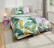 Bett mit Wendebettwäsche in tropischem Blattdesign, fotografiert aus einer seitlichen Perspektive.
