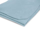 Weiche, hellblaue Decke aus Fleece mit gesticktem Logo, perspektivisch von oben fotografiert.