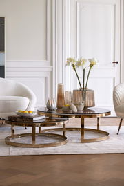 Moderner Couchtisch im Set mit zwei runden Tischen, goldene Metallrahmen und dunkle Glasplatten, dekoriert mit Vasen und Blumen, seitliche Perspektive.