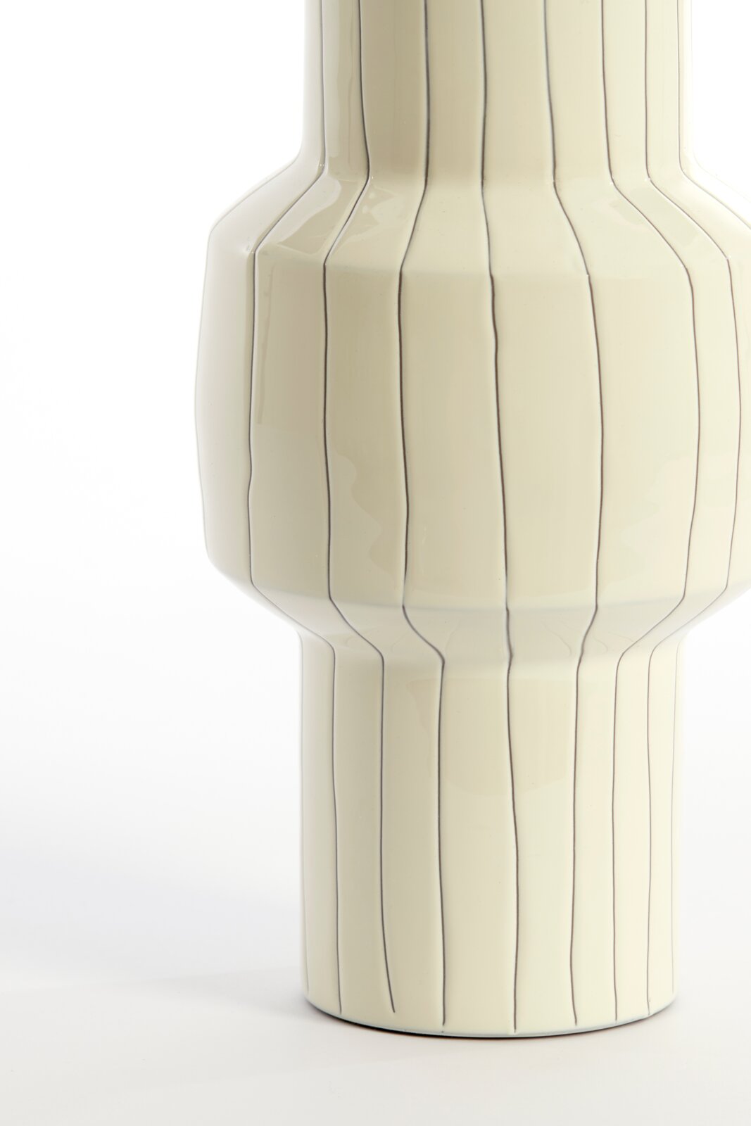 Nahaufnahme aus frontaler Perspektive einer cremefarbenen Keramikvase mit glänzender Oberfläche, markanter Silhouette und feinen, unregelmäßigen Längslinien.