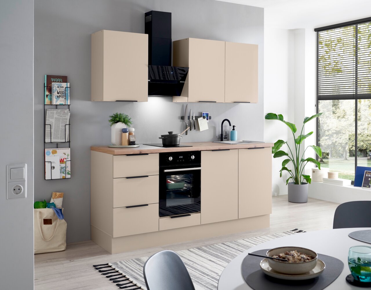 Moderne keukenblok in beige met houten werkblad, zwarte handgrepen, ingebouwde oven, kookplaat, spoelbak en zwarte afzuigkap, van voren gefotografeerd vanuit een licht schuin perspectief