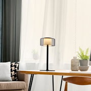 Moderne Tischleuchte RIKA auf einem Tisch in einem gemütlichen Wohnzimmer, seitliche Perspektive.