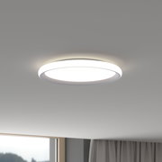 Runde, flache LED-Deckenleuchte in Weiß an der Zimmerdecke, eingeschaltet und mit gleichmäßigem warmweißem Licht; Ansicht leicht von unten in einem Wohnraum.