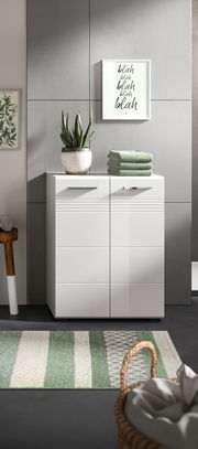 Moderner weißer Midischrank mit zwei Türen, dekoriert mit einem Pflanzentopf und gefalteten Handtüchern, aus frontaler Perspektive.