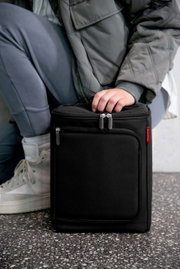 Schwarze Kühltasche mit Reißverschluss, von einer Person in grauer Kleidung gehalten, seitliche Perspektive.