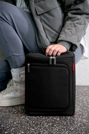 Schwarze Kühltasche mit Reißverschluss, von einer Person in grauer Kleidung gehalten, seitliche Perspektive.