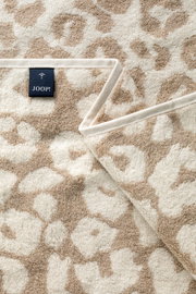 Close-up van een beige saunadoek met bloemenpatroon en een Joop-label.