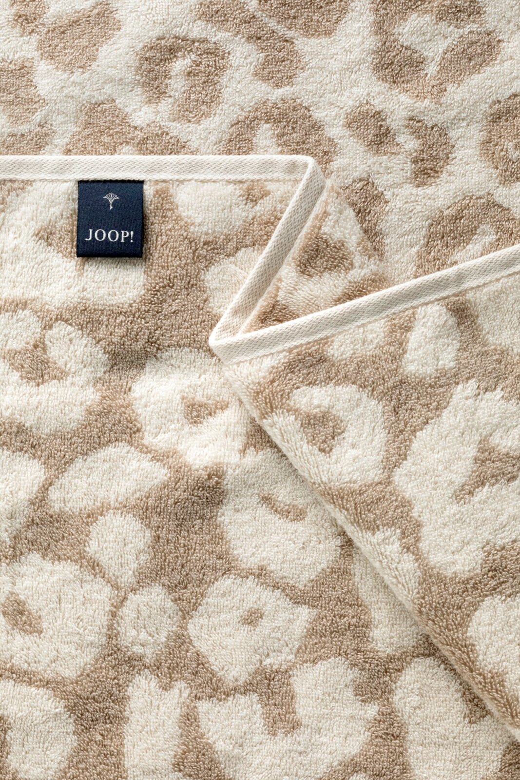 Close-up van een beige saunadoek met bloemenpatroon en een Joop-label.