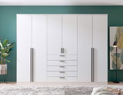 6-türiger Drehtürenschrank in Weiß mit schwarzen Griffen, frontal fotografiert, vor einer grünen Wand mit Pflanzen und Dekoration.