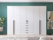 6-türiger Drehtürenschrank in Weiß mit schwarzen Griffen, frontal fotografiert, vor einer grünen Wand mit Pflanzen und Dekoration.