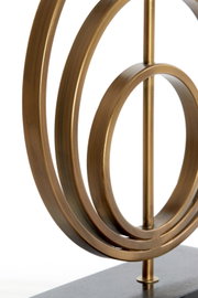 Close-up van een decoratieve lampvoet van metaal met cirkelvormige elementen in een gouden kleur, gezien vanaf de zijkant.