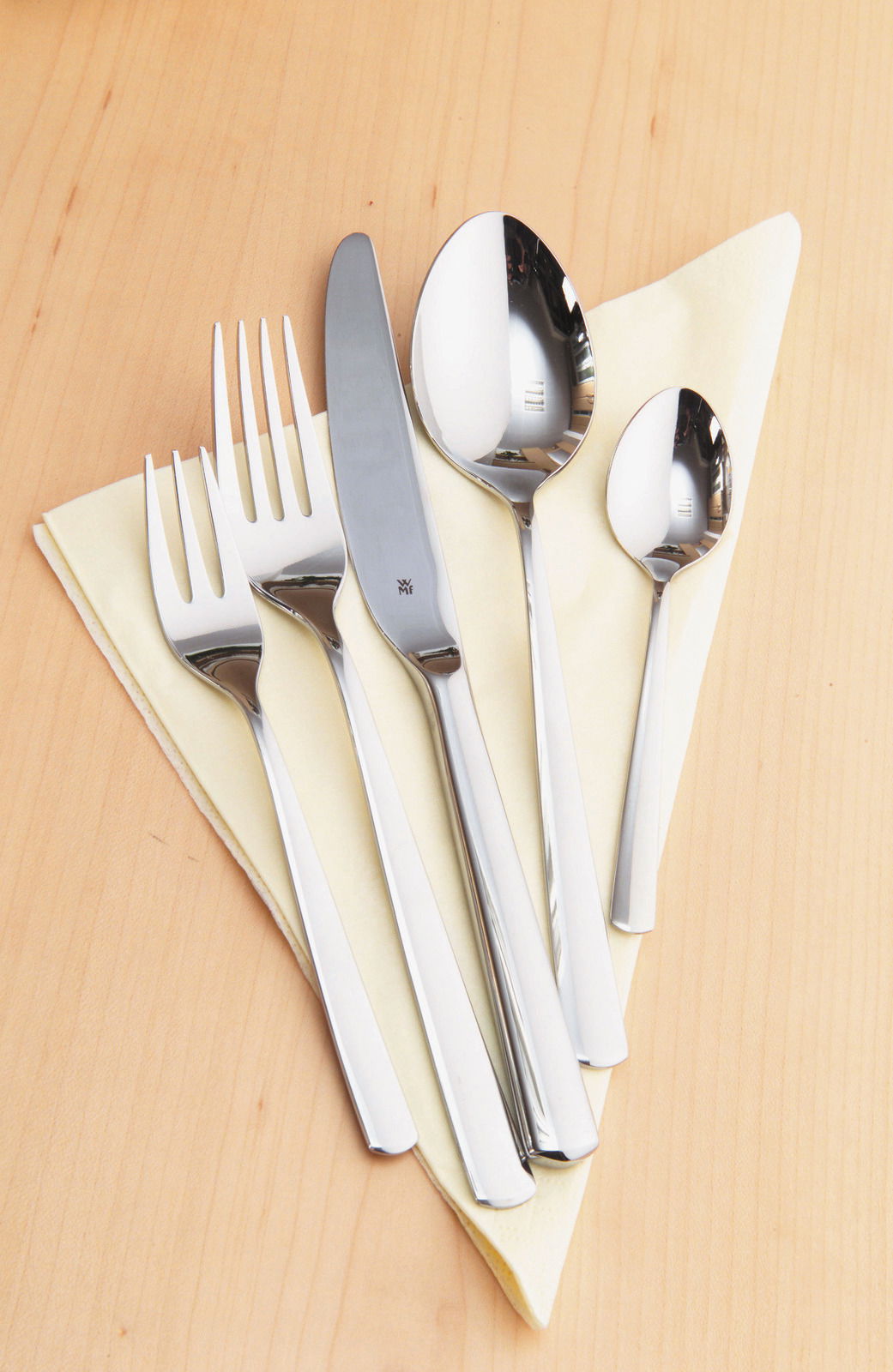 WMF Besteckset 30-tlg. BOSTON Besteckset Boston 30-tlg. aus Edelstahl, bestehend aus Messer, Gabel, Esslöffel und Teelöffel, auf einem hellen Holzuntergrund mit gelber Serviette, von oben fotografiert.