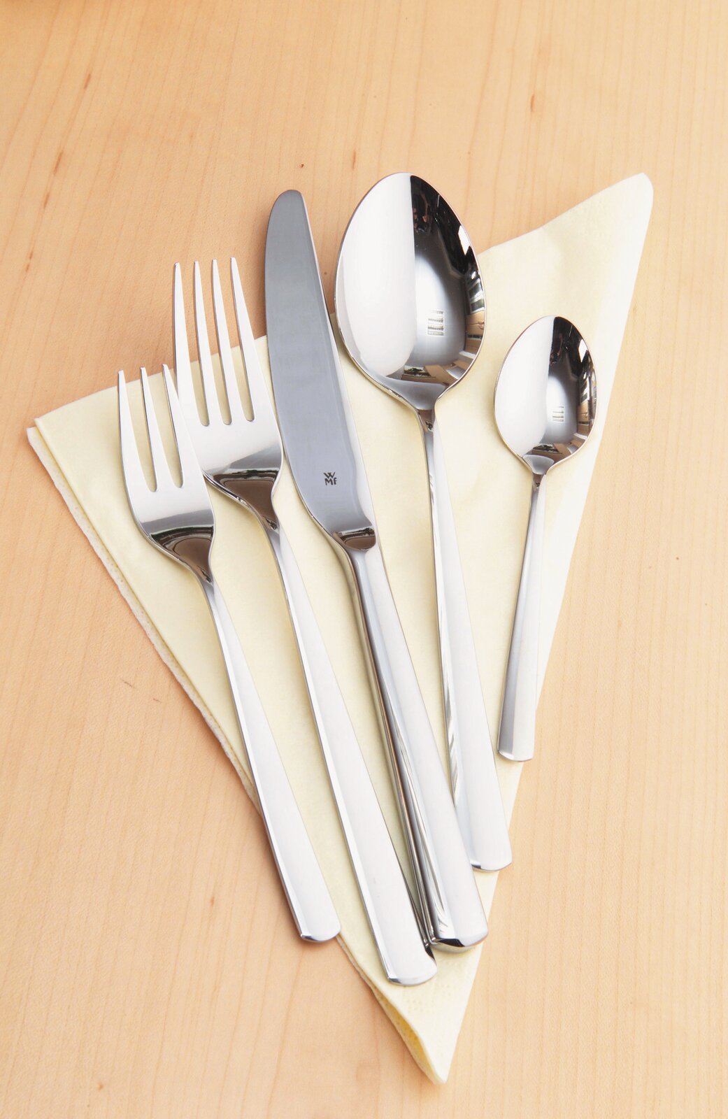 Besteckset Boston 30-tlg. aus Edelstahl, bestehend aus Messer, Gabel, Esslöffel und Teelöffel, auf einem hellen Holzuntergrund mit gelber Serviette, von oben fotografiert.