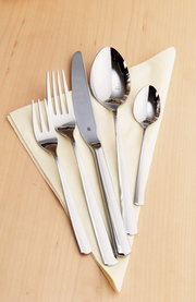 Besteckset Boston 30-tlg. aus Edelstahl, bestehend aus Messer, Gabel, Esslöffel und Teelöffel, auf einem hellen Holzuntergrund mit gelber Serviette, von oben fotografiert.