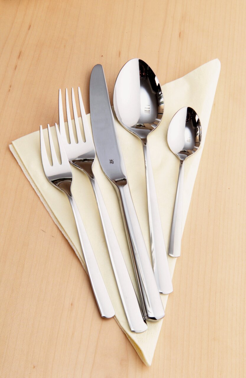 Besteckset Boston 30-tlg. aus Edelstahl, bestehend aus Messer, Gabel, Esslöffel und Teelöffel, auf einem hellen Holzuntergrund mit gelber Serviette, von oben fotografiert.