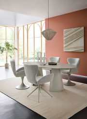 Moderner Essbereich mit ovalem Tisch und vier gepolsterten Armlehnstühlen in einem hellen Raum mit großen Fenstern. Perspektive von der Seite.