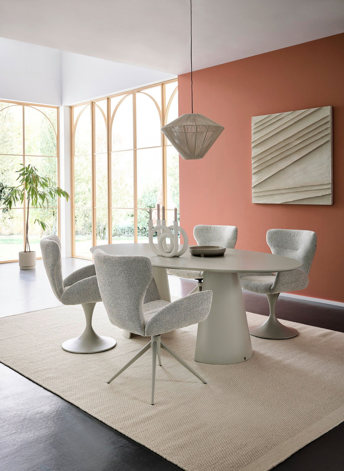 Moderner Essbereich mit ovalem Tisch und vier gepolsterten Armlehnstühlen in einem hellen Raum mit großen Fenstern. Perspektive von der Seite.