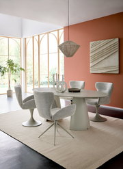 Moderner Essbereich mit ovalem Tisch und vier gepolsterten Armlehnstühlen in einem hellen Raum mit großen Fenstern. Perspektive von der Seite.