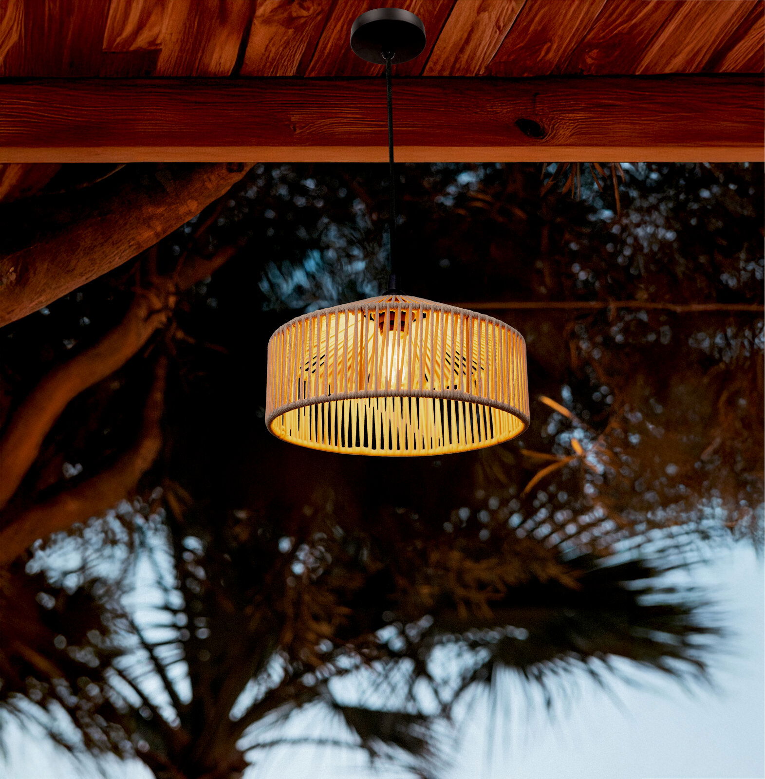 Hängelampe mit zylindrischem, naturfarbenem Rattan-/Bambus-Lampenschirm und warmem Licht, an schwarzem Kabel unter einer Holzdecke im Außenbereich, fotografiert in leichter Untersicht.