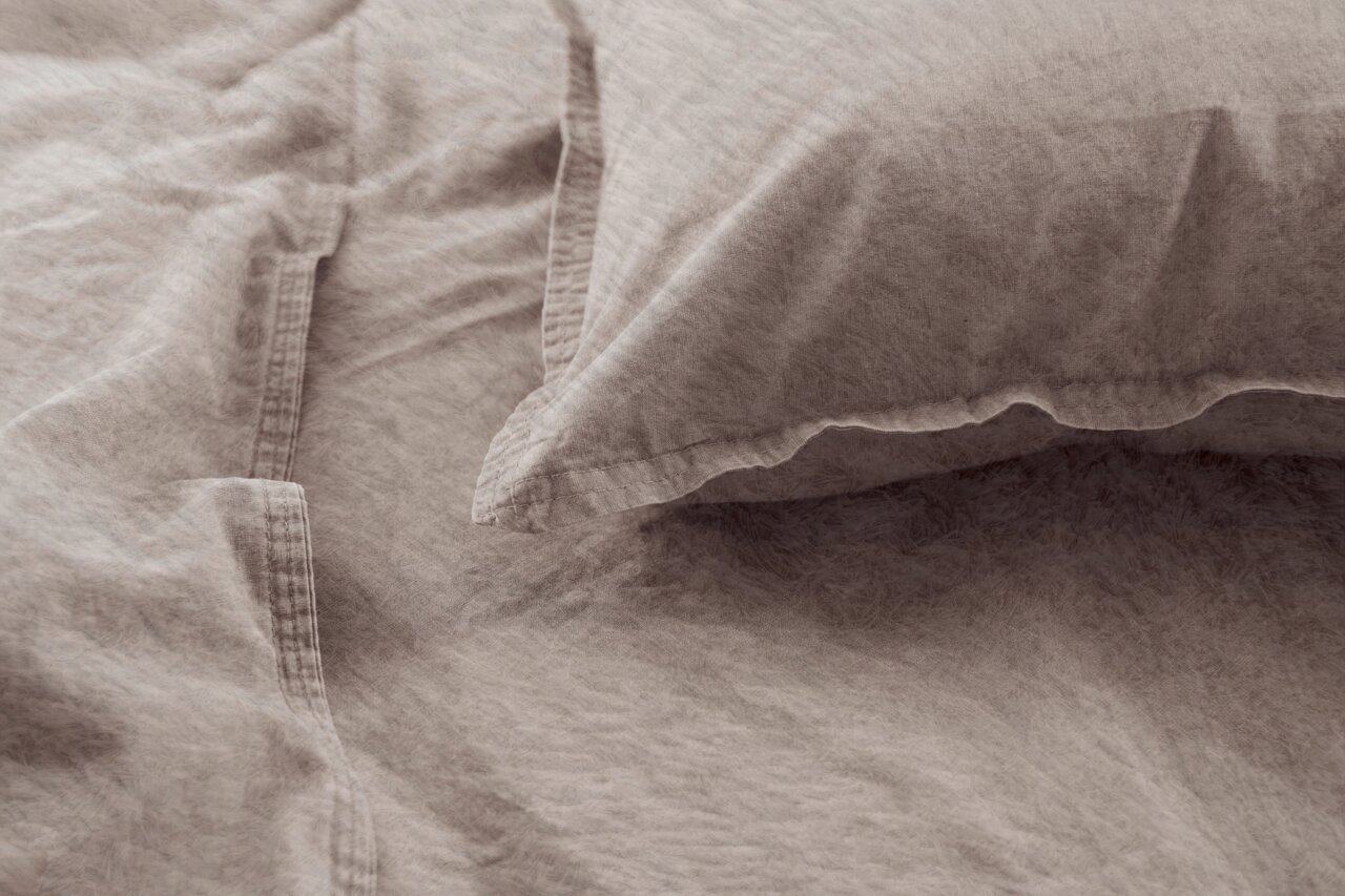 Nahaufnahme einer Bettwäsche in Beige mit Kissenbezug, aus der Vogelperspektive fotografiert.