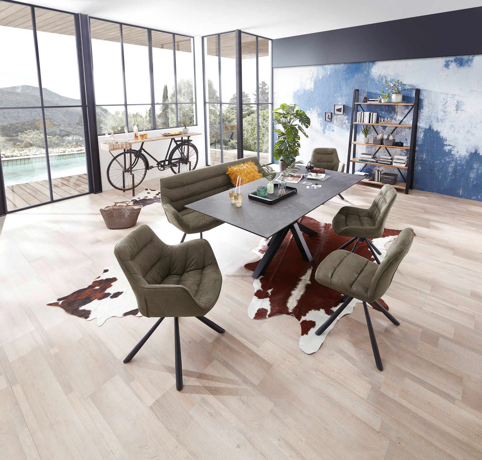 Moderner Essbereich mit großem Esstisch und grünen Stühlen, umgeben von großen Fenstern mit Blick auf die Natur. Perspektive von oben.