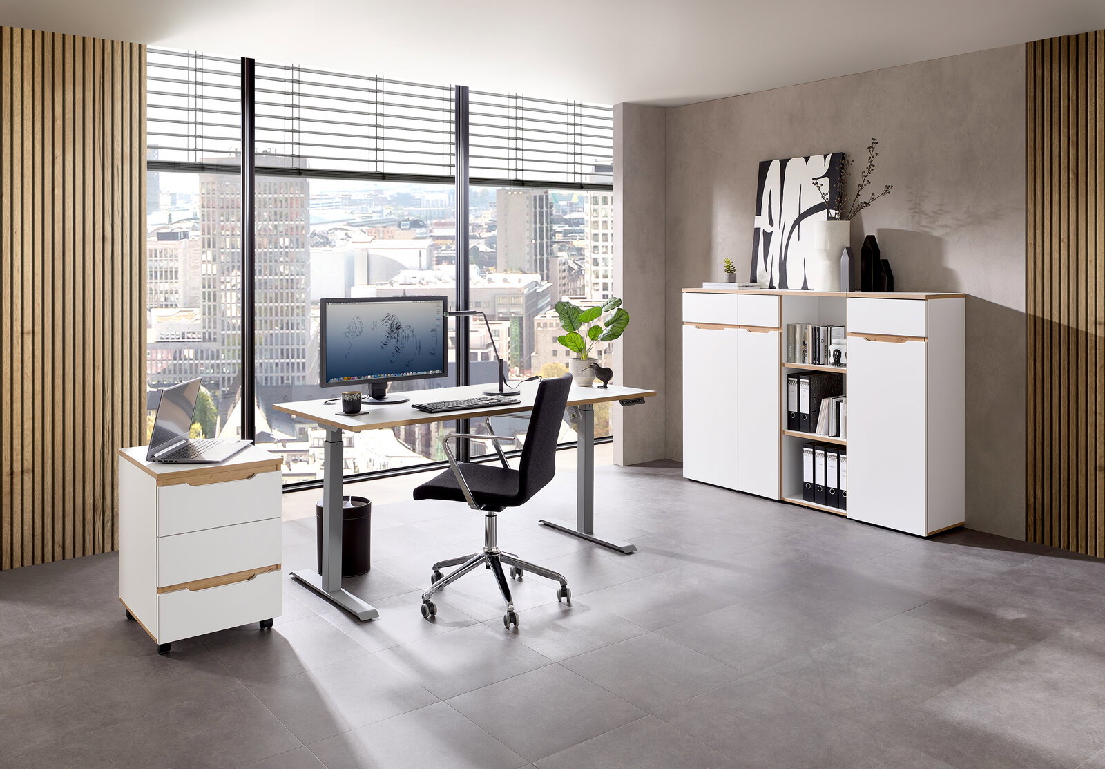 Voleo E-Schreibtisch DETROIT Modernes Büro mit einem höhenverstellbaren Schreibtisch, einem Rollcontainer und einem Aktenschrank, mit Blick auf die Stadt durch große Fenster.