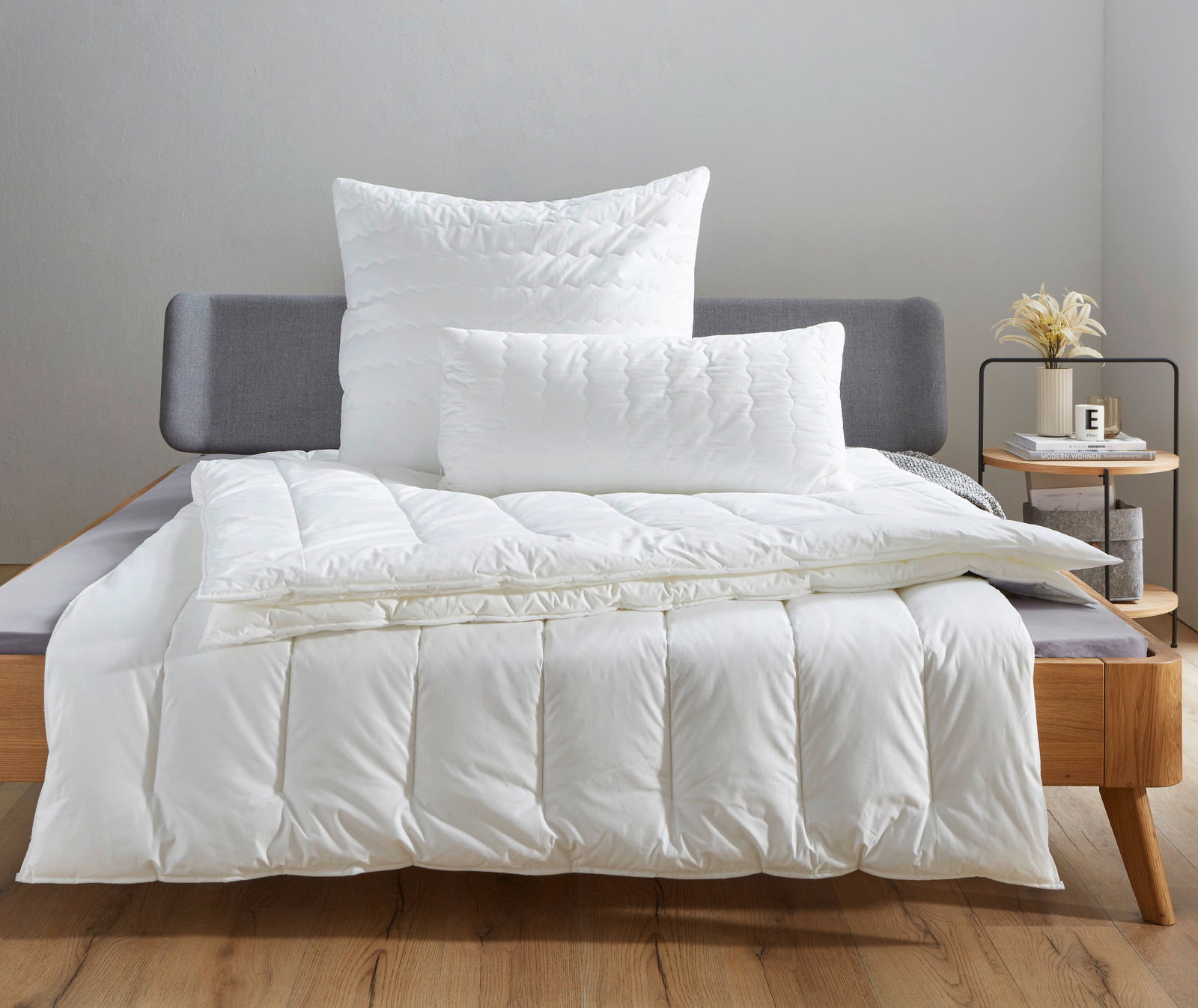 Ganzjahresbett Centa Star Inspiration in einem modernen Schlafzimmer, frontal fotografiert, mit weißen Kissen und Decke auf einem grauen Bett.