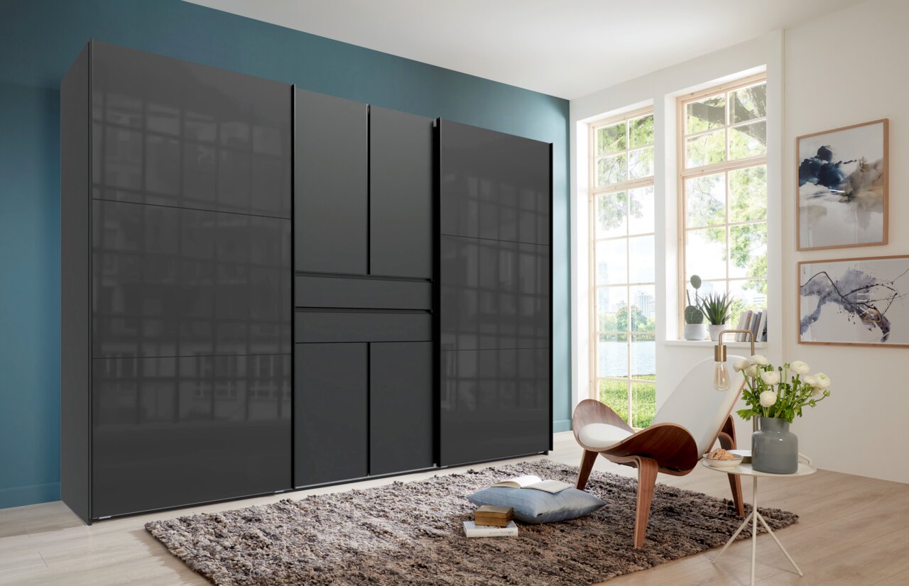 Großer, moderner Kleiderschrank mit hochglänzender dunkelgrauer Front und mehreren Türen in einem hellen Schlafzimmer, perspektivisch in leichter Schrägansicht von vorn links.