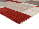 Nahaufnahme eines mehrfarbigen Teppichs mit geometrischem Muster in Rot-, Beige- und Grautönen, perspektivisch von der Seite aufgenommen.