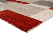 Nahaufnahme eines mehrfarbigen Teppichs mit geometrischem Muster in Rot-, Beige- und Grautönen, perspektivisch von der Seite aufgenommen.