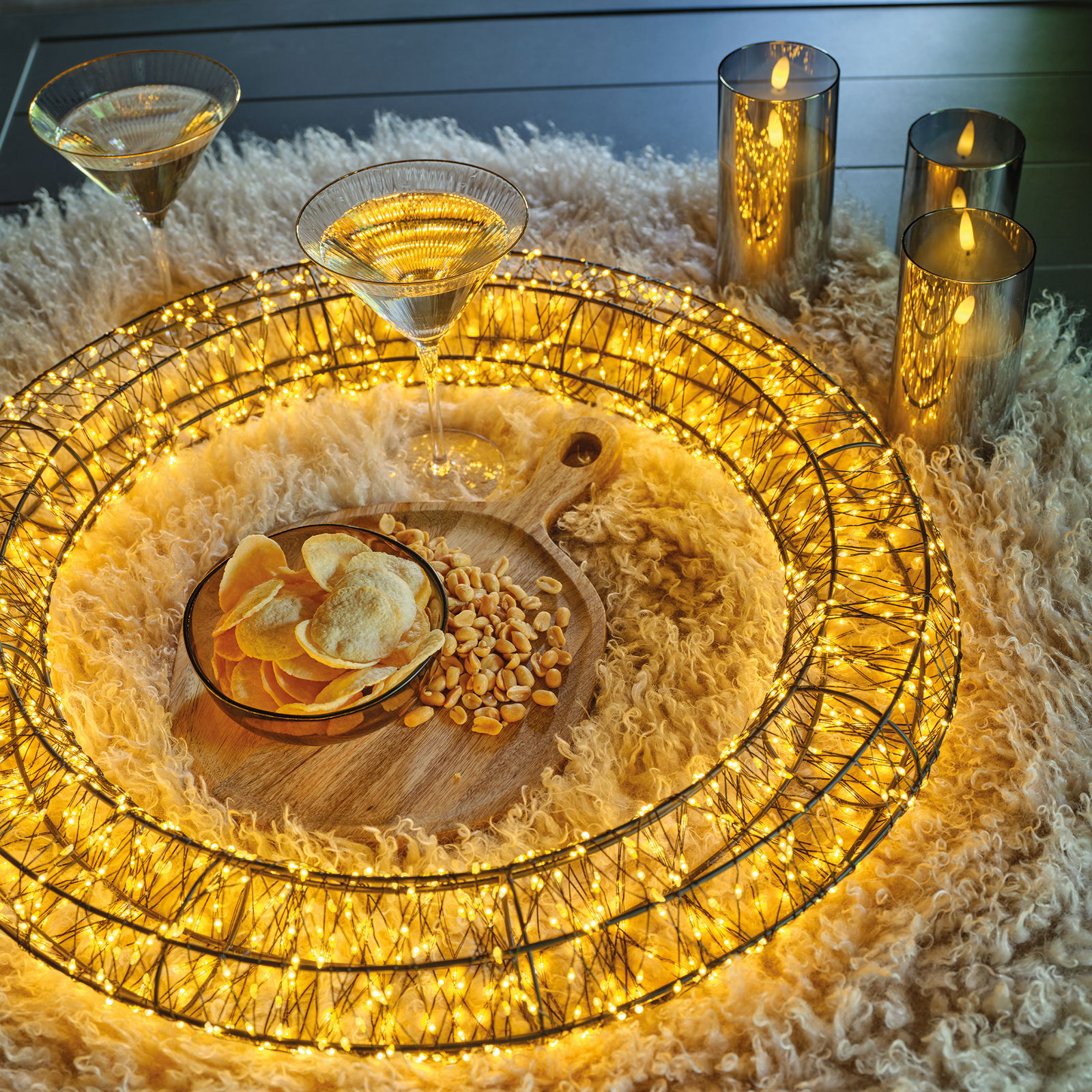 LED-Kranz mit warmweißen Lichtern, umgeben von Kerzen und Snacks auf einem flauschigen Teppich, aus der Vogelperspektive.