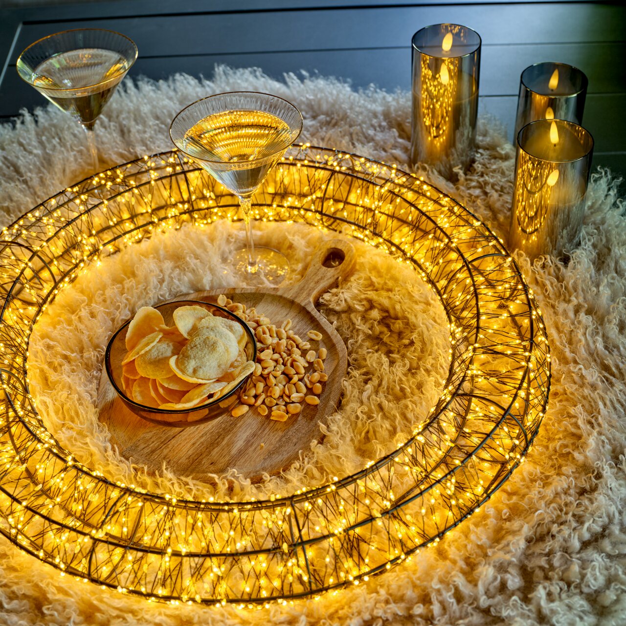 LED-Kranz mit warmweißen Lichtern, umgeben von Kerzen und Snacks auf einem flauschigen Teppich, aus der Vogelperspektive.