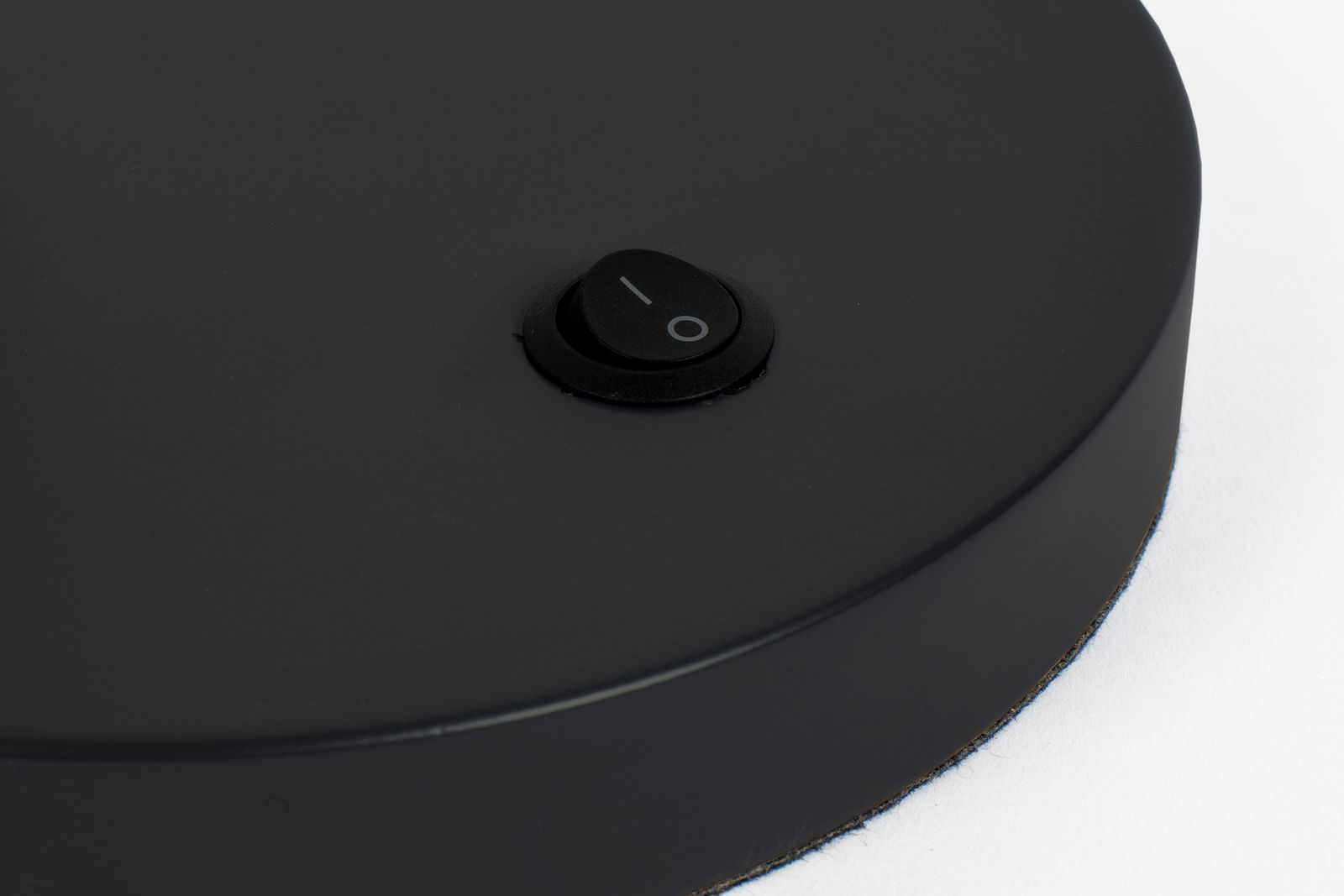 Nahaufnahme eines schwarzen Schalters auf der Basis einer Schreibtischleuchte, von oben betrachtet.