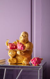 Goldene Gorilla-Dekofigur als Butler mit Tablett und Drachenfrüchten, seitliche Perspektive.