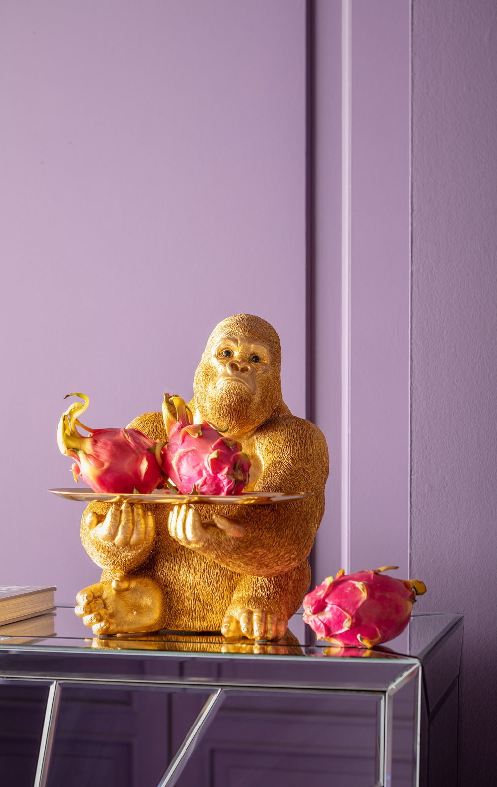 Goldene Gorilla-Dekofigur als Butler mit Tablett und Drachenfrüchten, seitliche Perspektive.