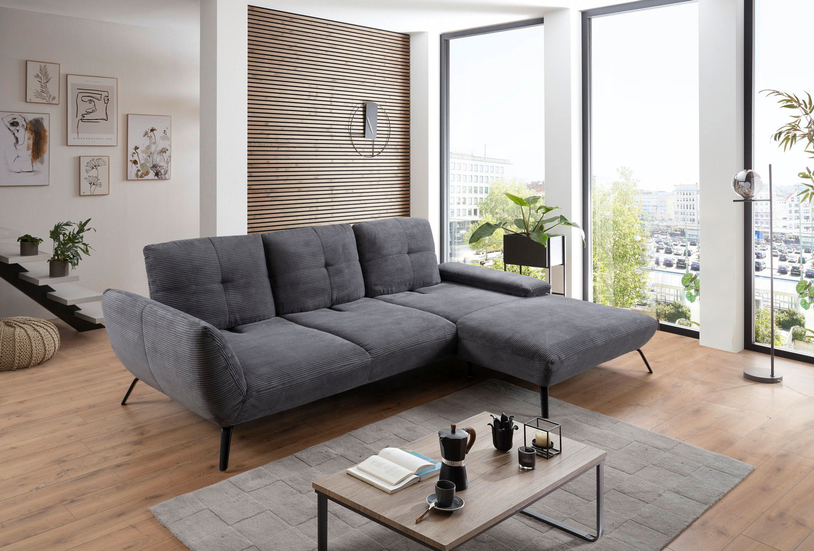 Graues Ecksofa in modernem Wohnzimmer mit Holzboden und großen Fenstern, seitliche Perspektive