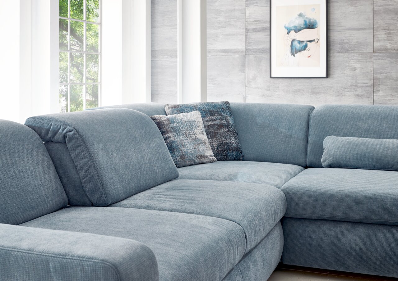 Blaue Polsterrundecke in einem modernen Wohnzimmer, seitliche Perspektive mit dekorativen Kissen und einem großen Fenster im Hintergrund.