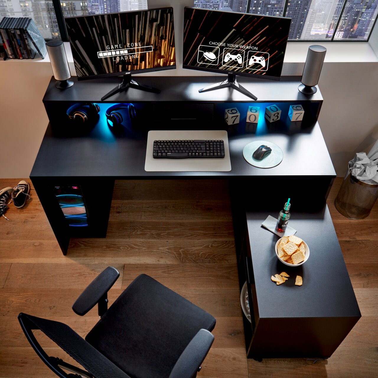 Gaming-Schreibtisch mit zwei Monitoren, Tastatur und Maus aus der Vogelperspektive, umgeben von Kopfhörern, Lautsprechern und Snacks.