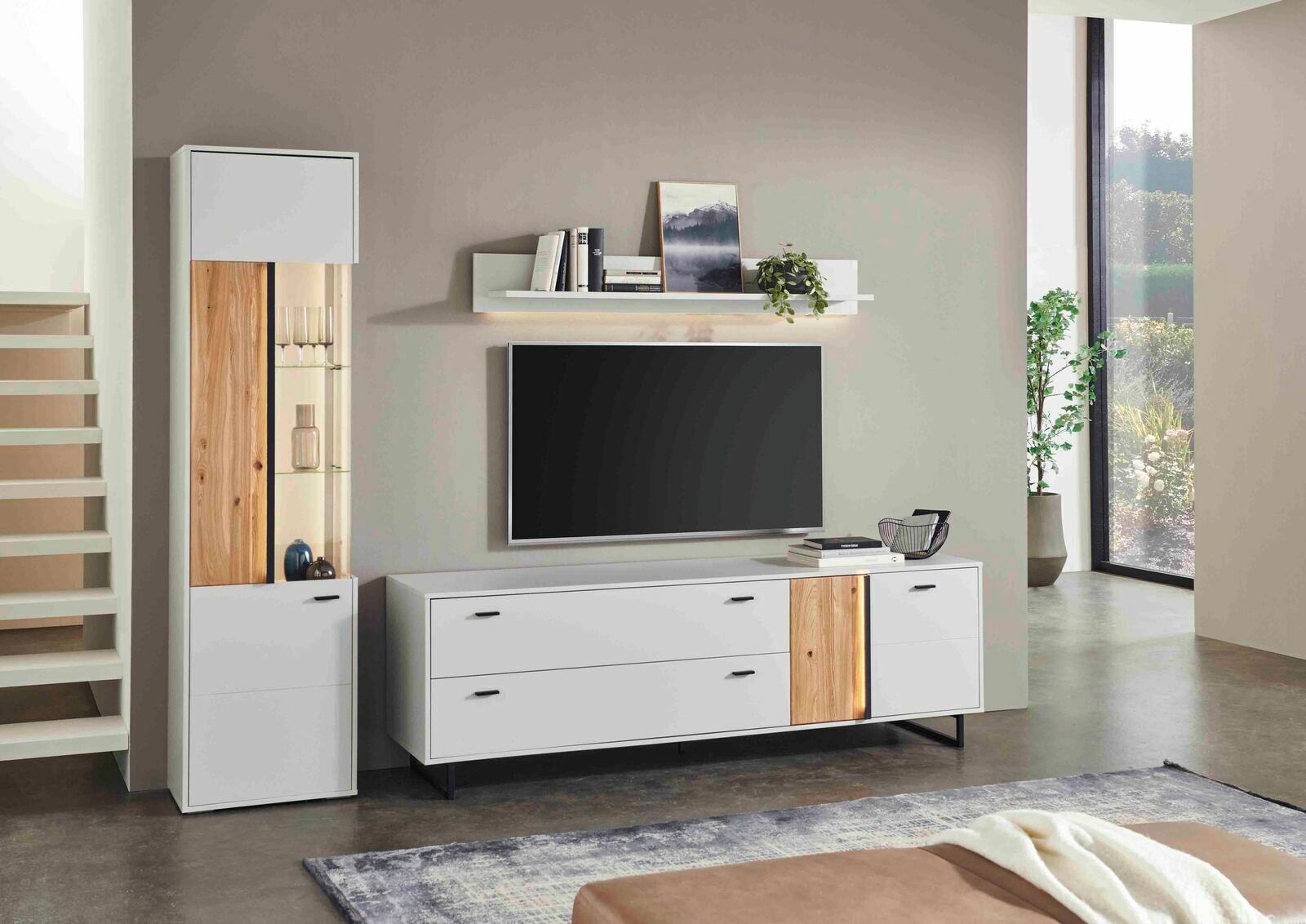 Moderne Wohnzimmer-Vitrine in Weiß mit Holzelementen, links im Bild, neben einem TV-Schrank. Frontale Perspektive.