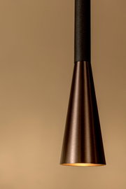 Nahaufnahme einer konischen Pendelleuchte aus gebürstetem Metall in Bronze-/Kupferton mit warmem Lichtaustritt, frontal von unten fotografiert vor beigem Hintergrund