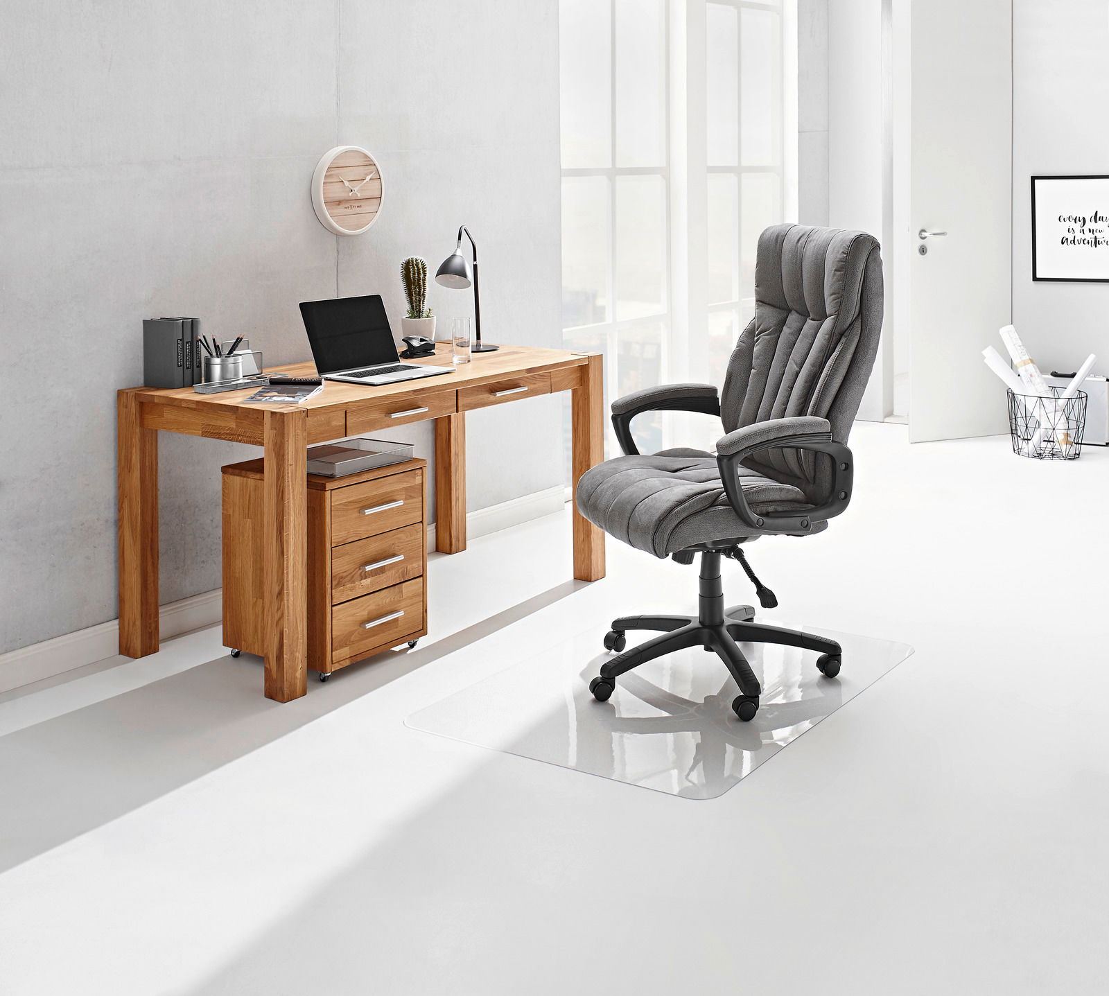 Moderner Schreibtisch aus Holz mit Schubladen, seitliche Perspektive, ausgestattet mit Laptop, Lampe und Büromaterialien, daneben ein grauer Bürostuhl auf einer transparenten Bodenmatte.
