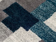 Nahaufnahme eines Frisé-Teppichs mit geometrischem Muster in Grau, Blau und Weiß.