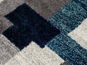 Nahaufnahme eines Frisé-Teppichs mit geometrischem Muster in Grau, Blau und Weiß.